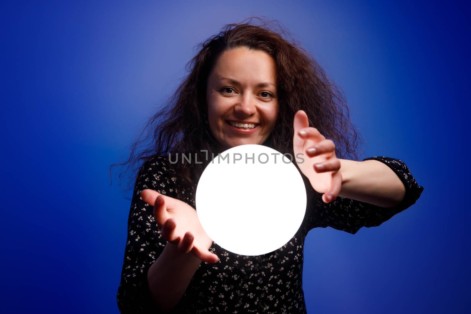 Smiling girl holding a glowing ball in her hands. Blue background