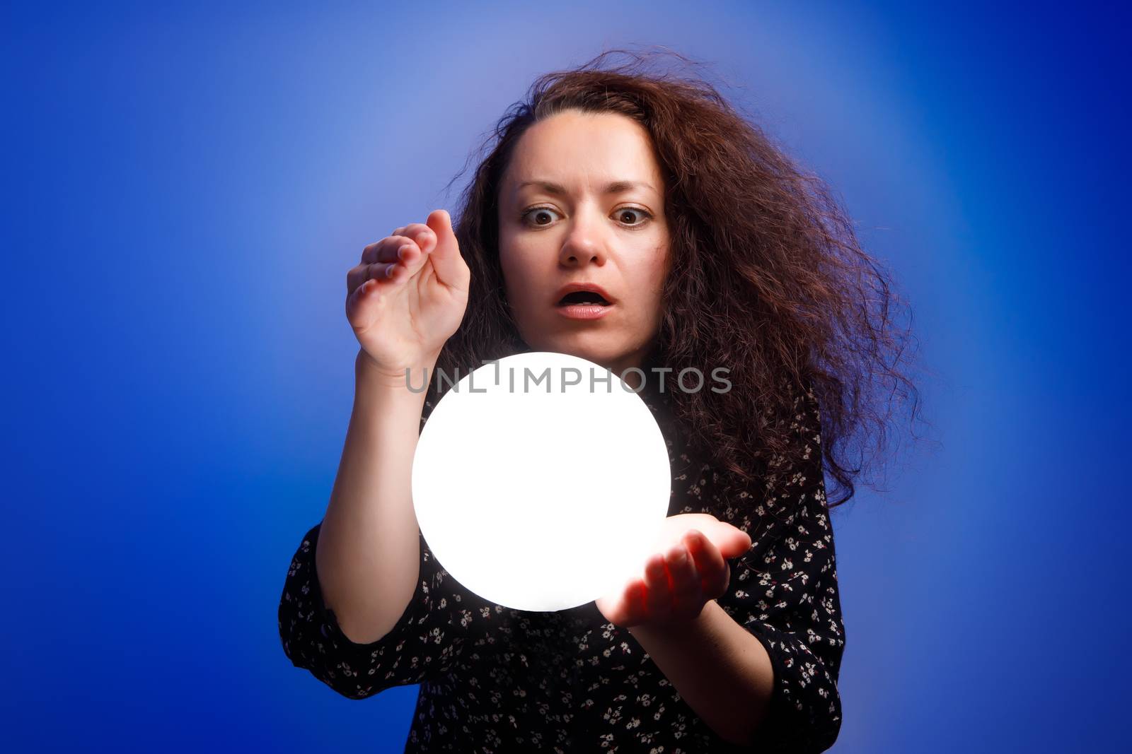 Smiling girl holding a glowing ball in her hands. Blue background. by 9parusnikov