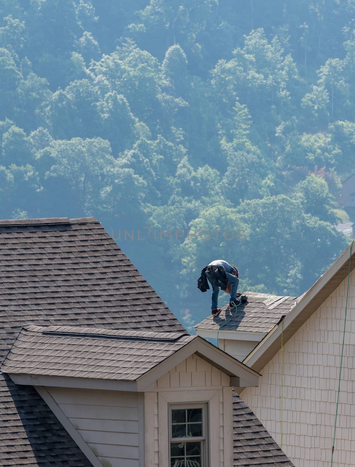 Young roofing contractor replacing the old shingles on a townhouse roof high above the ground