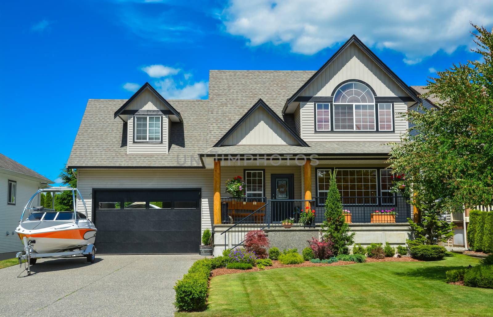 Suburban house with landscaping in front and blue sky background. Light powerboat parked on concrete driveway in front of the house