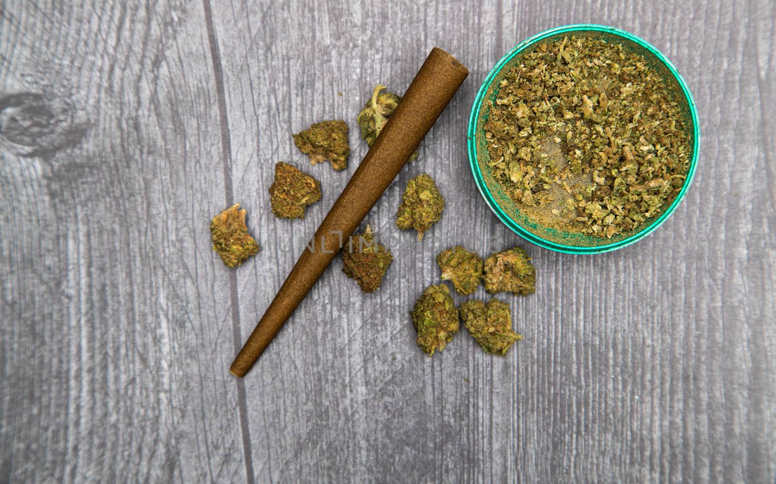 Large green buds of medical marijuana sit on a wooden table with a hemp wrap and grinder.