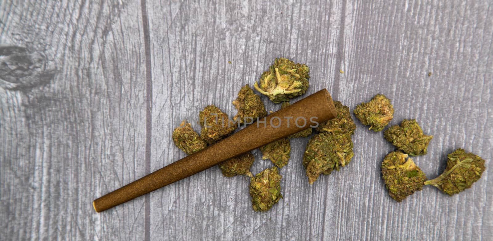 Large green buds of medical marijuana sit on a wooden table with a hemp wrap, ready to be smoked.