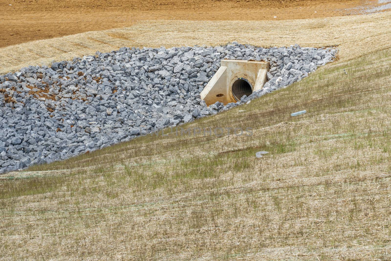 Horizontal shot of a culvert and drainage ditch under construction.  

Drainage ditch pipe in background.