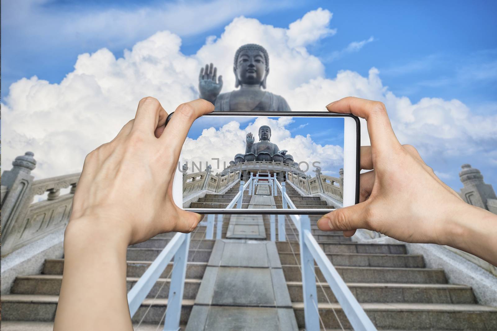 Girl taking pictures on mobile smart phone in Tian Tan Giant Buddha on big cloud background