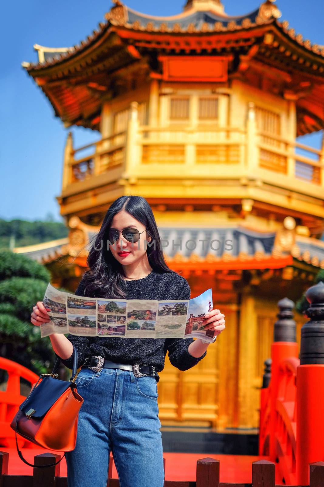 Young female tourist with map looking for a way to Gold Chinese pavilion Temple at the park in Hong Kong
