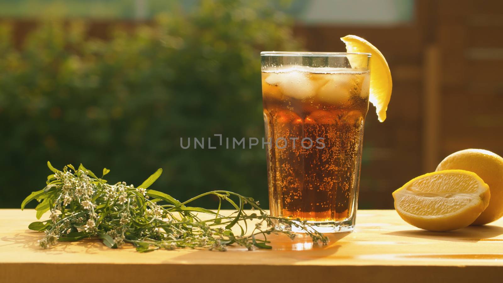 Close up glass of sparkling drink with lemon and ice on the table in the garden. Refreshing drink. Summer still life