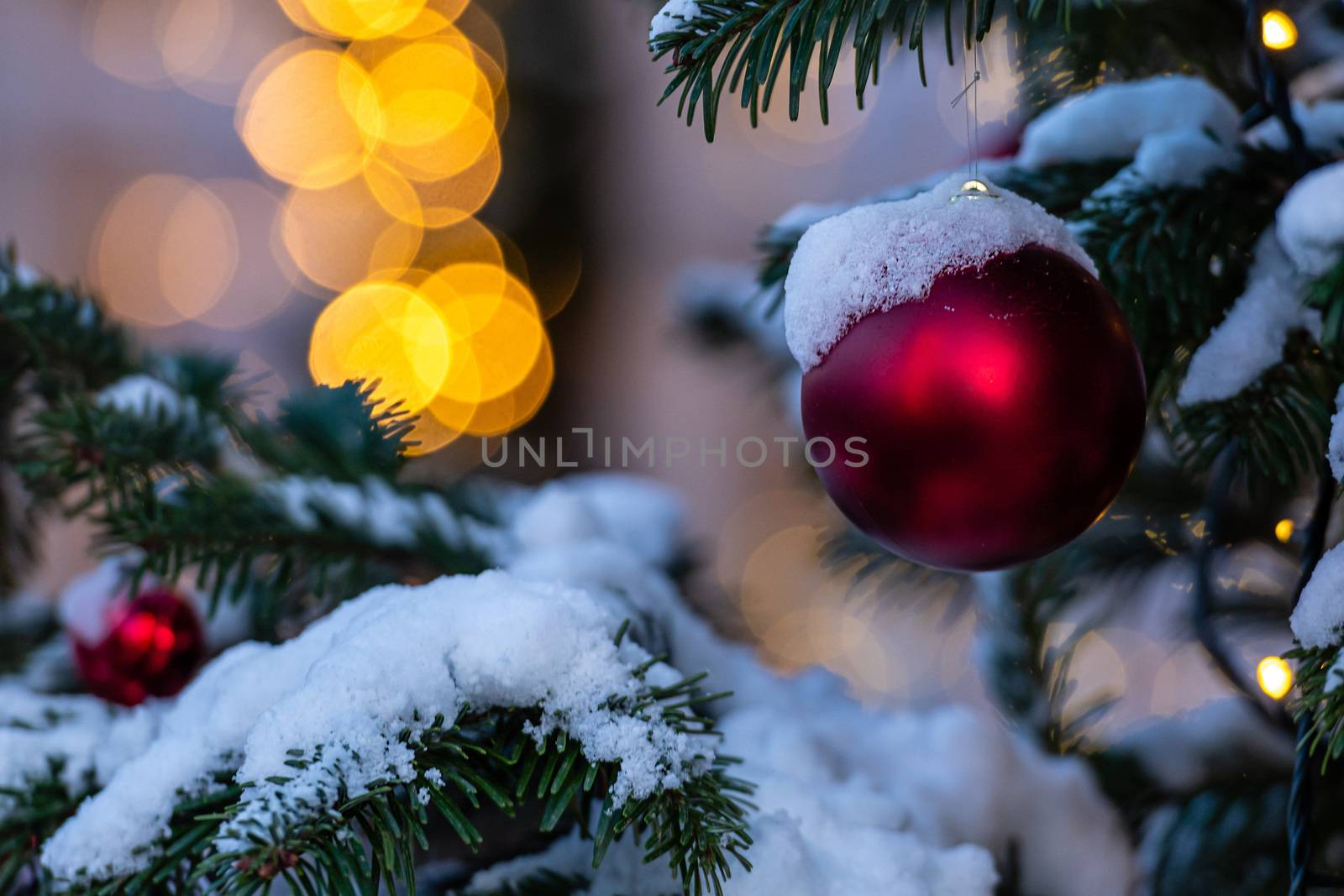 Colorful decorations on snow-covered Christmas tree branches. Defocused background with Christmas lights - image