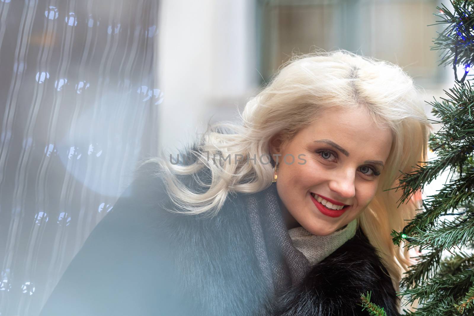 Portrait of a young smiling blonde woman photographed through the Christmas lights, soft focus - image