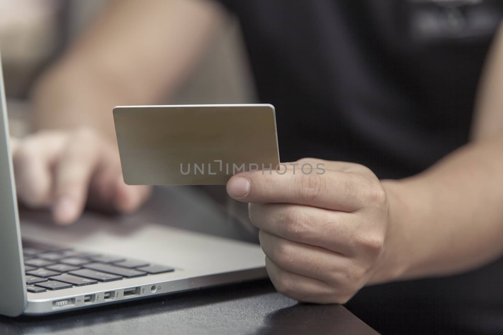 The man with a plastic card sits at the laptop and makes purchase online