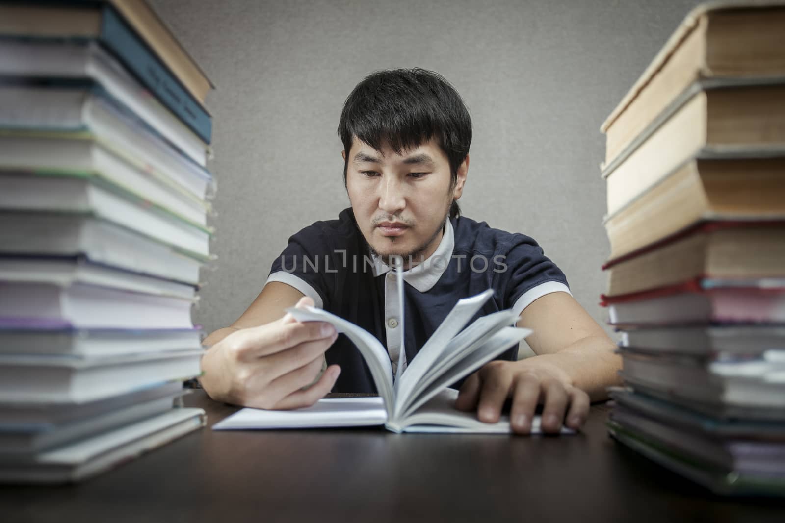 The young man looks at book on a table between textbooks