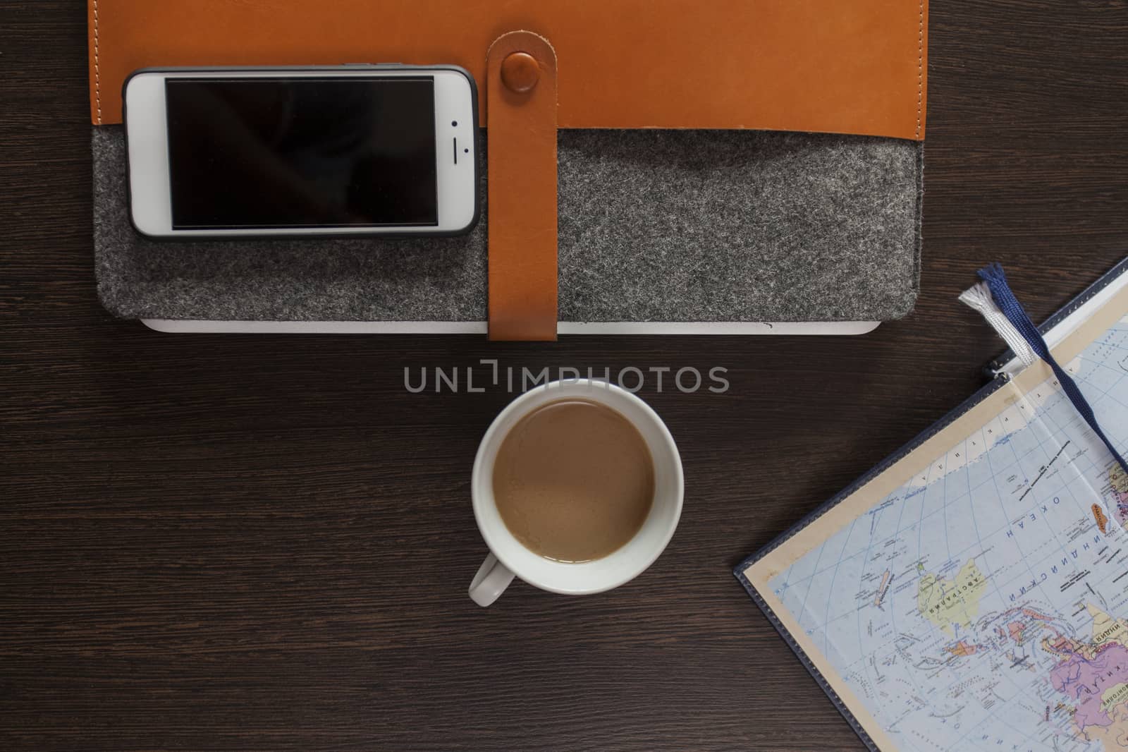 On a wooden table a laptop in a cover, the smartphone, a cup of coffee and a notebook