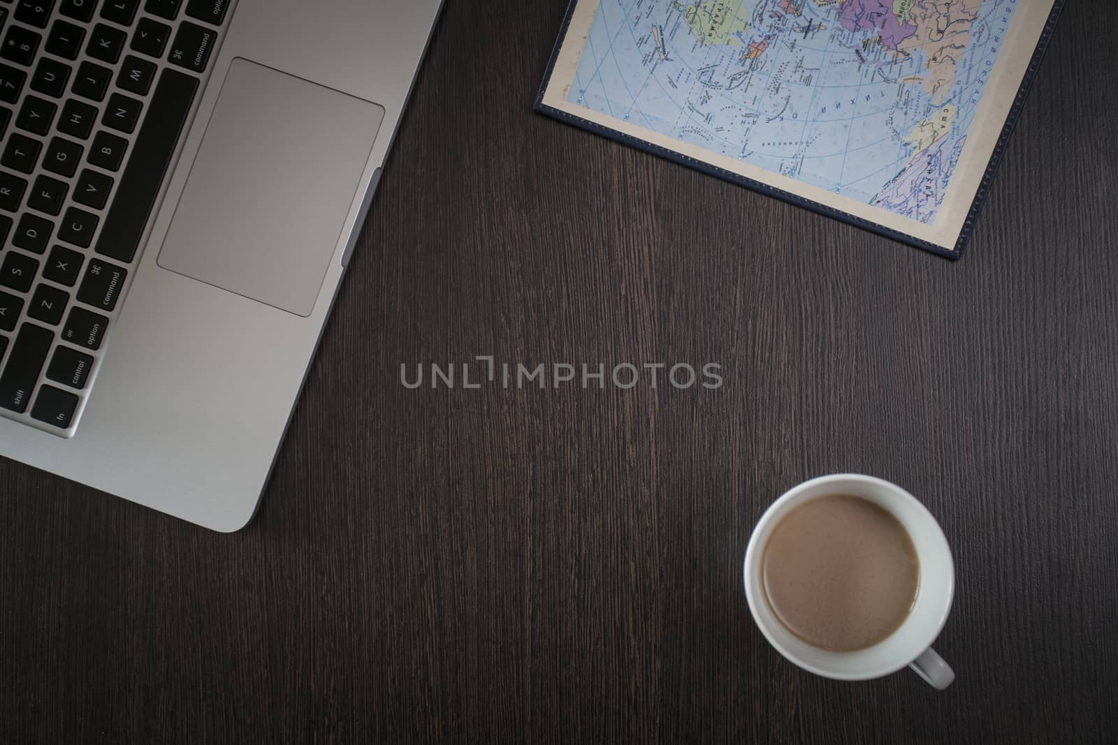 On a wooden table a laptop, a cup of coffee and a notebook