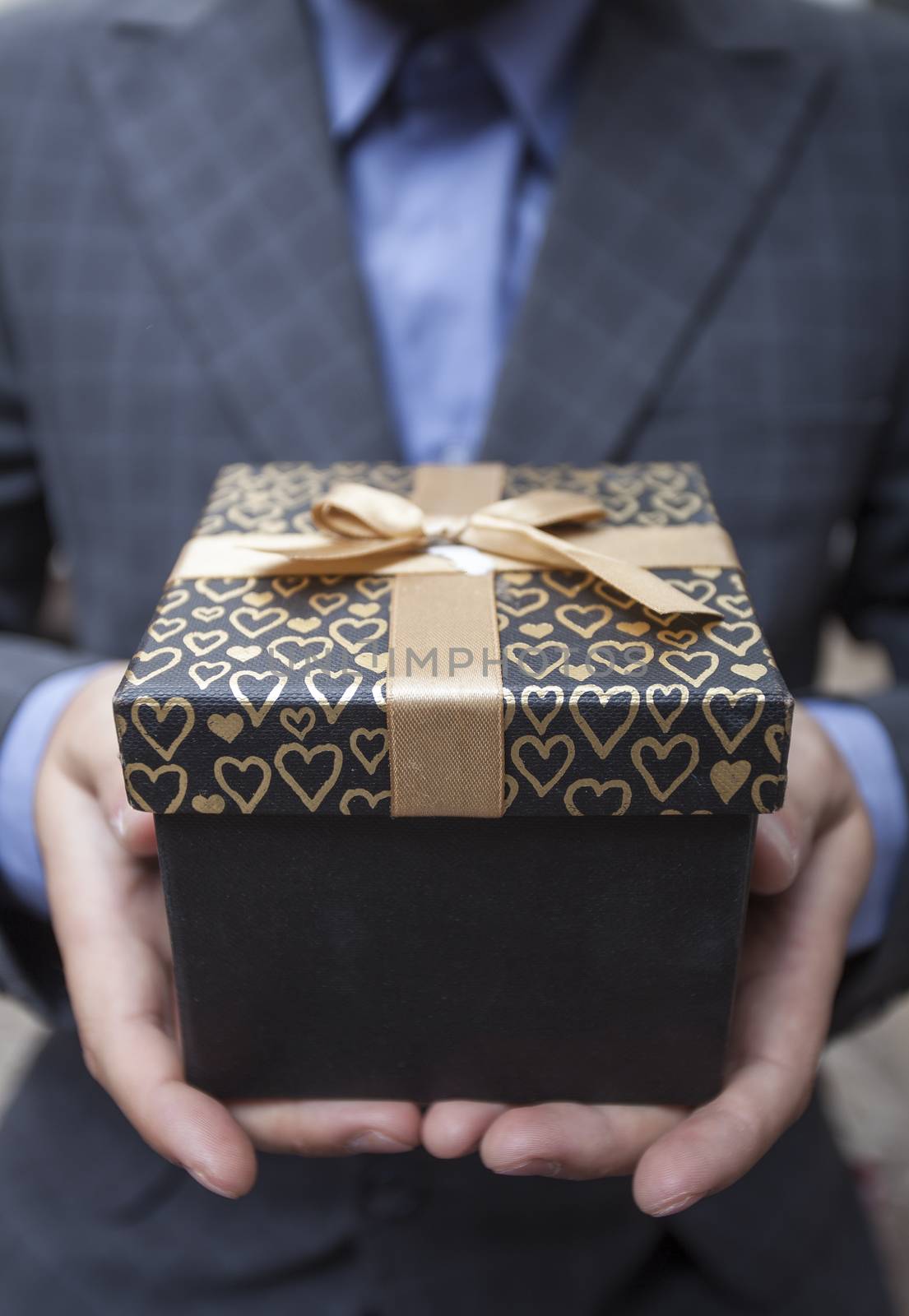 Man's hands keep a box in a business suit wrapped up by a bow