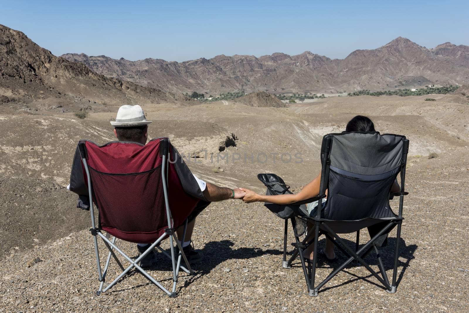 Couple in camping chairs over-looking a Wadi, mountains, in The United Arab Emirates