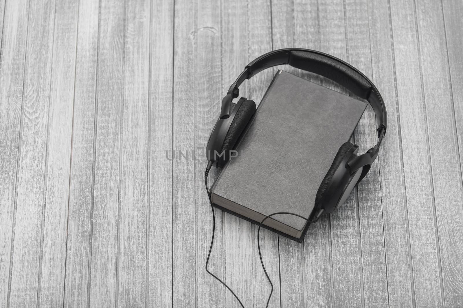 The book, big earphones lie on a wooden background, audiobooks
