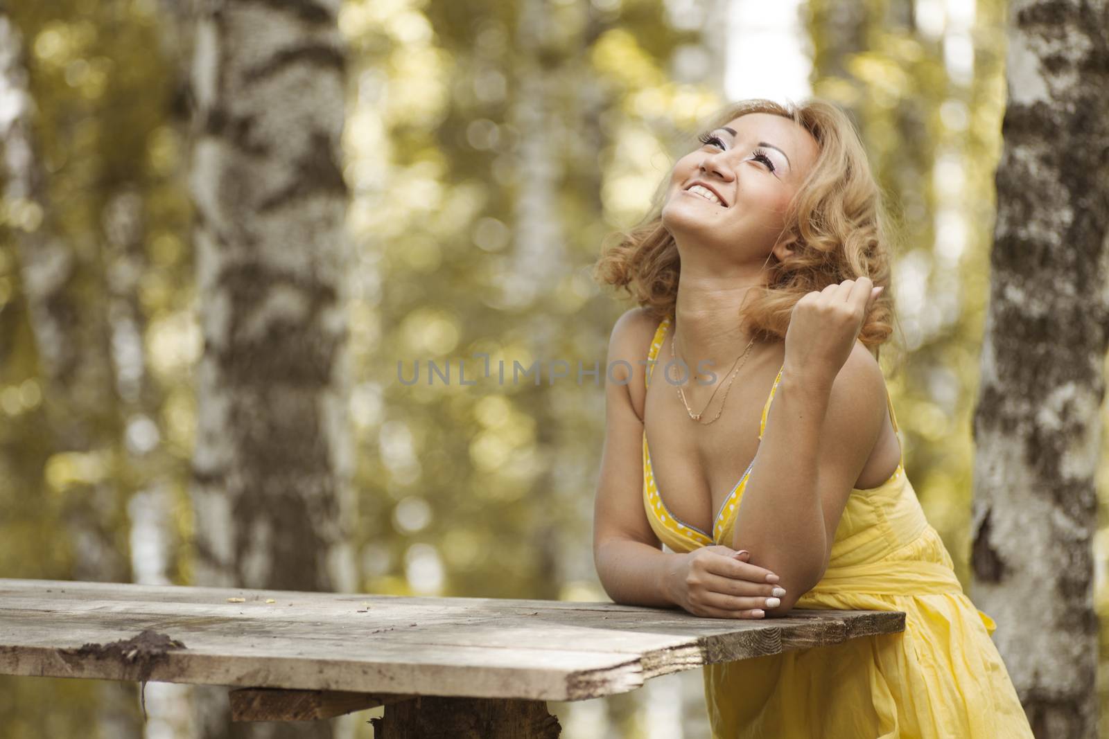 A girl in a yellow dress sitting in the woods behind a wooden table