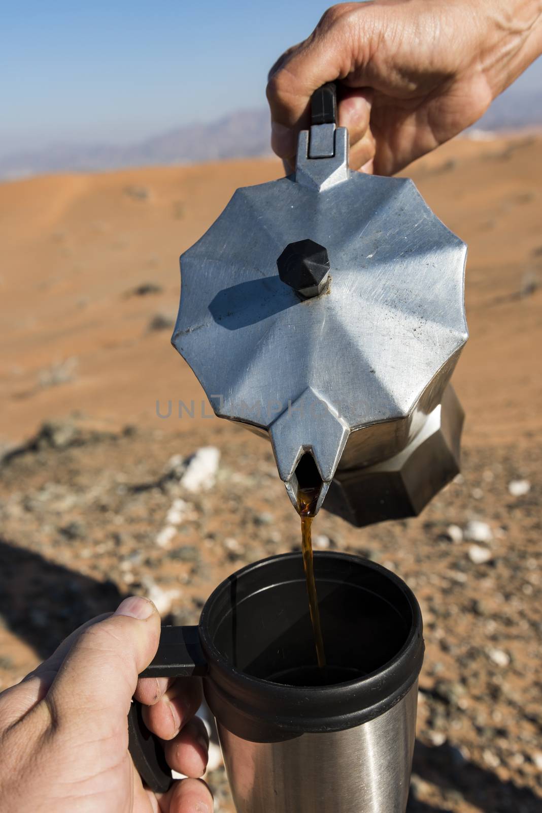 Woman Pouring coffee on a camping cup with the desert in background