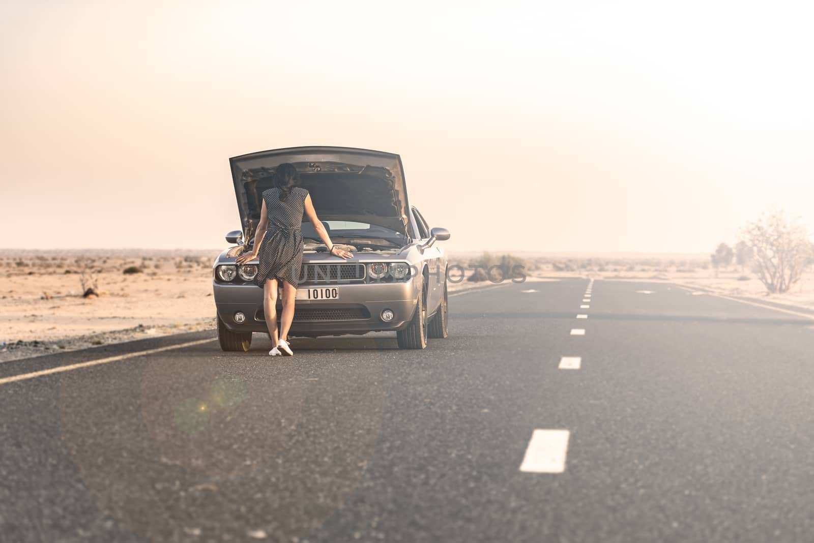 Woman looking to find the issue of the breakdown of her sport car on a road in the desert