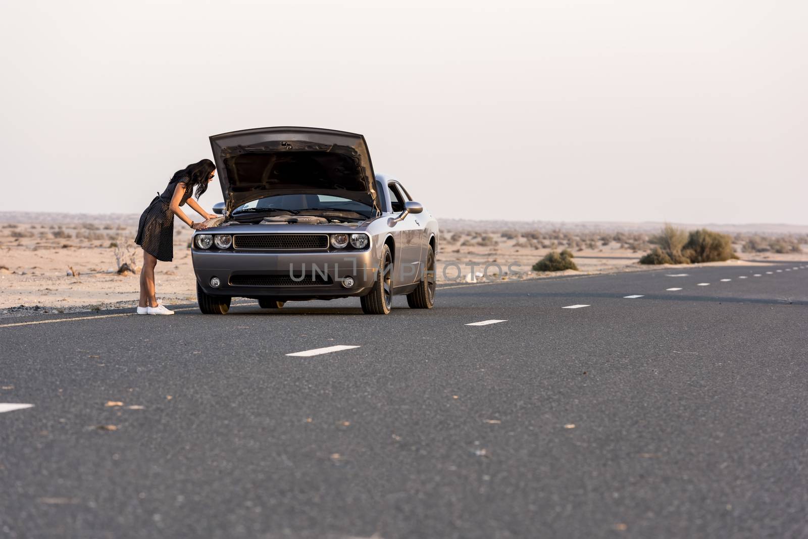 Car Breakdown with Woman checking the engine in the road in the middle of the desert