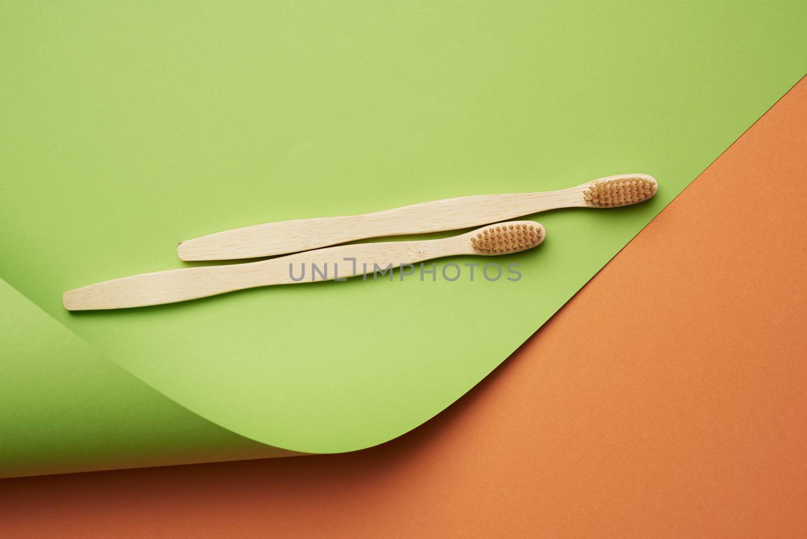 two wooden toothbrushes on a green orange background, plastic rejection concept, zero waste 