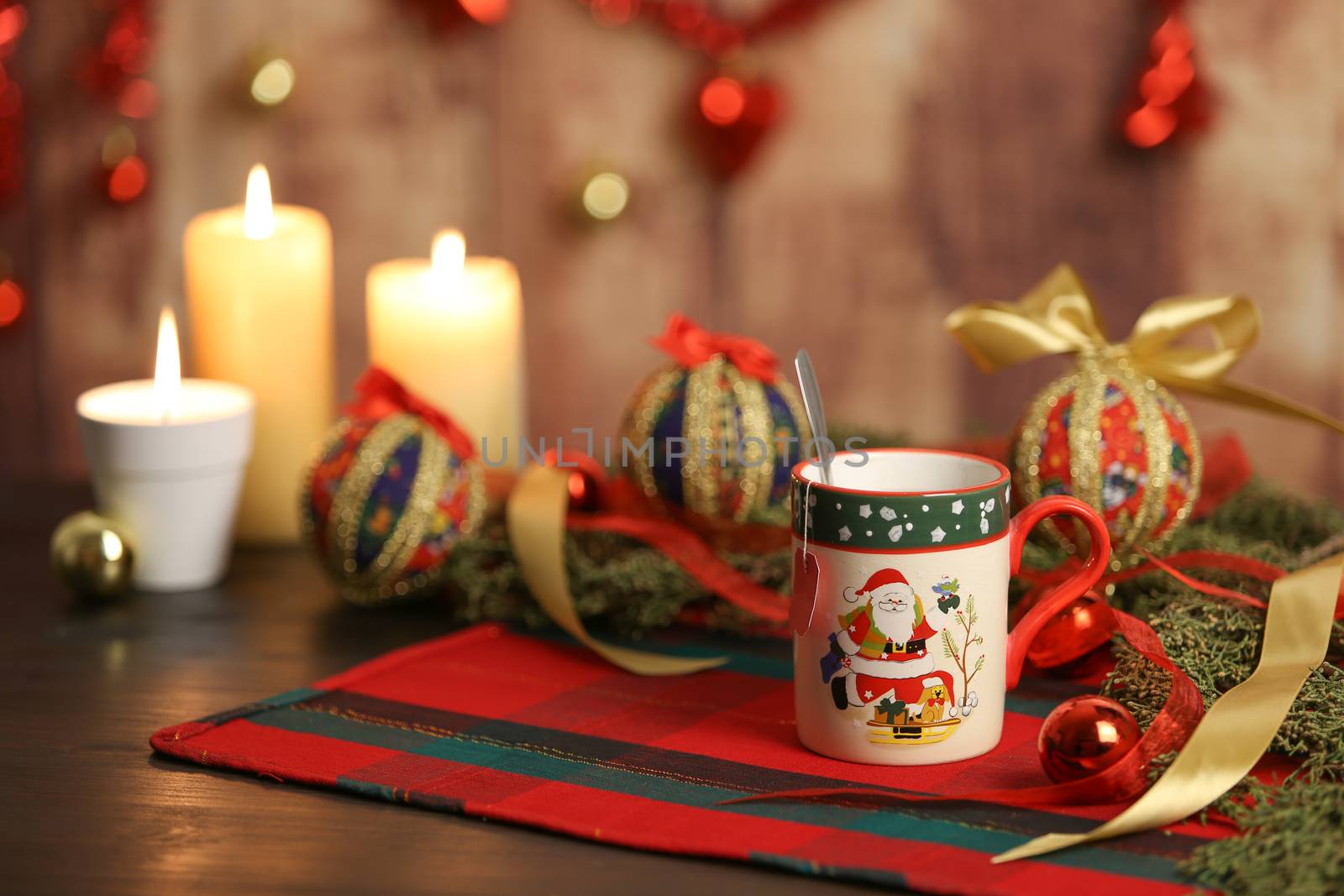 Christmas mug with empty tea label on Christmas table cloth with around pine branches, decoupage baubles, with lit candles and hanging Christmas decoration on wooden background with bokeh effect by robbyfontanesi