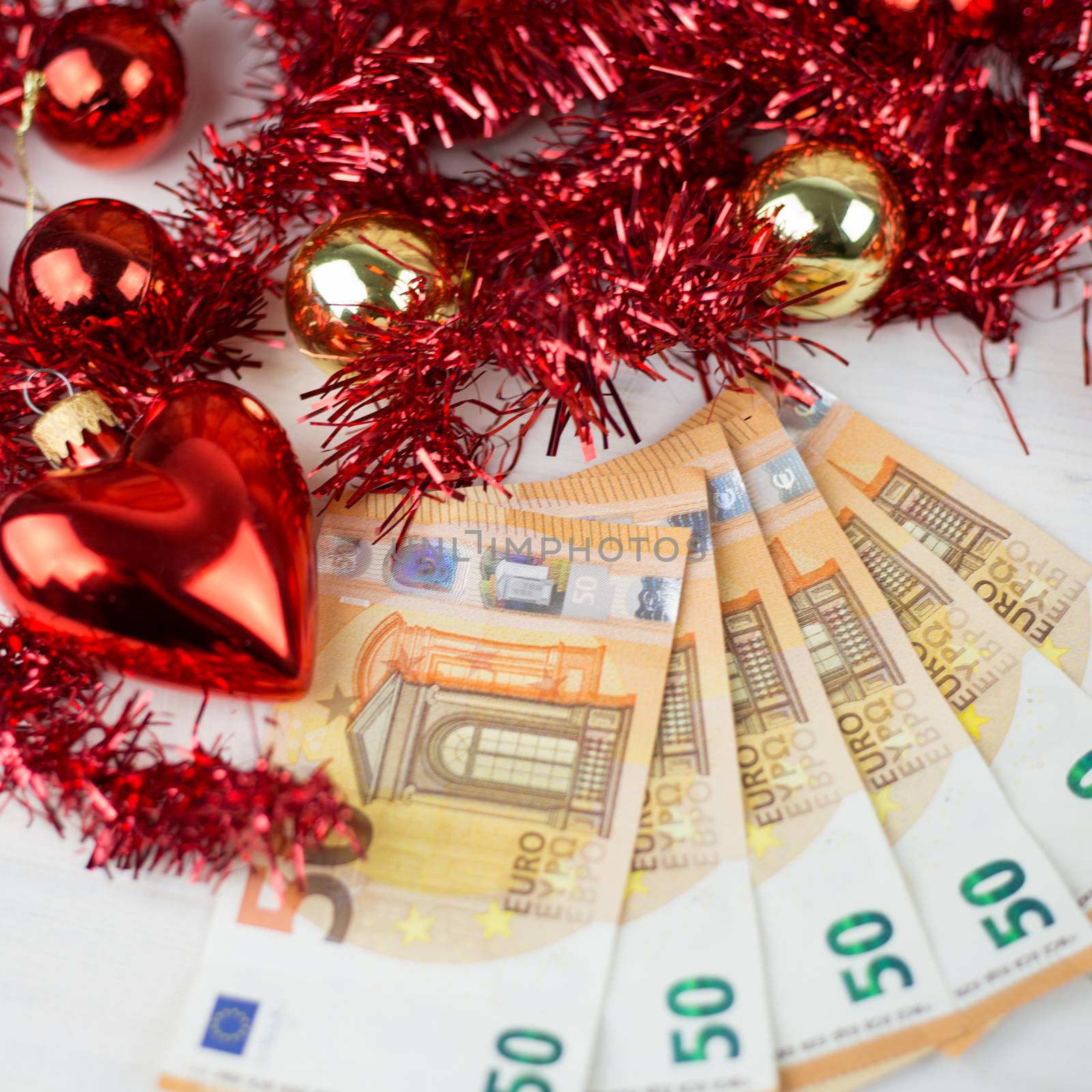 Christmas money business concept: some fifty euro banknotes with red and gold baubles and wreath decoration on light wooden table