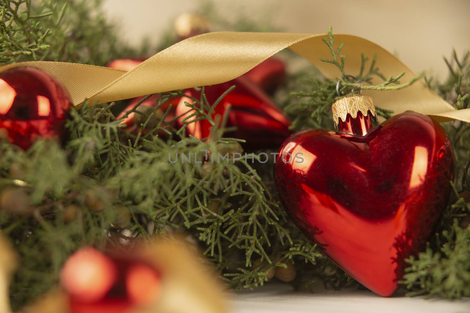 Close up of a Christmas red baubles with earth shape with around pine branches, red baubles and satin gold ribbon on wooden background with bokeh effect by robbyfontanesi