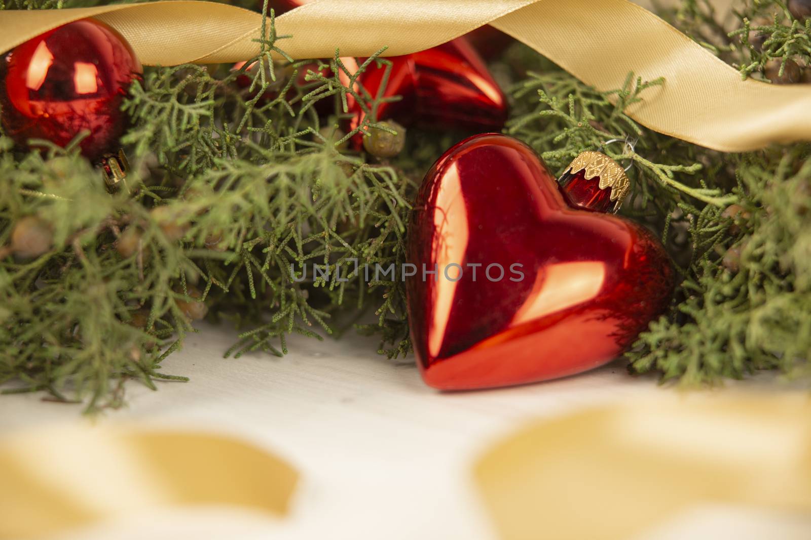 Close up of a Christmas red baubles with earth shape with around pine branches, red baubles and satin gold ribbon on wooden background with bokeh effect by robbyfontanesi