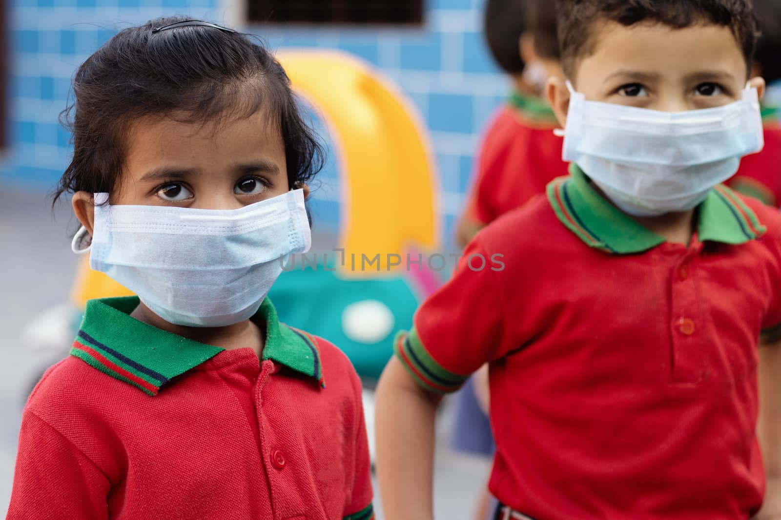 Little kids at school with medical face mask looking at camera - concept of kids using mask to protect from covid-19 or coronavirus spreading by lakshmiprasad.maski@gmai.com