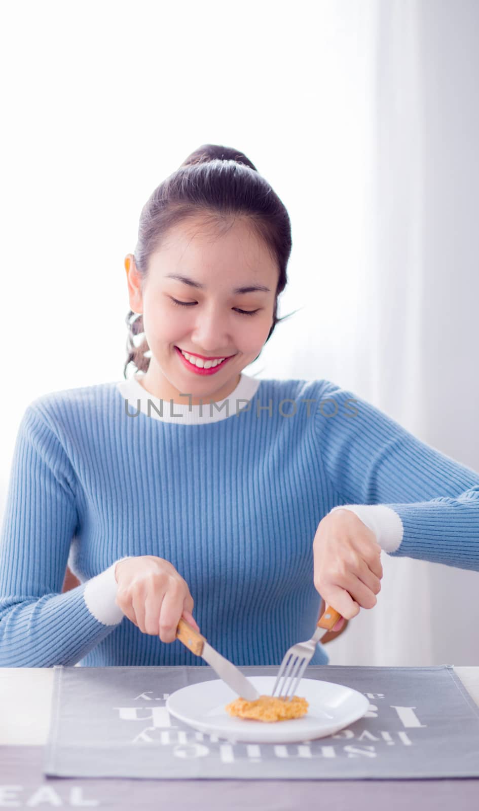 Pretty female hold spoon and knife eat food in kitchen.