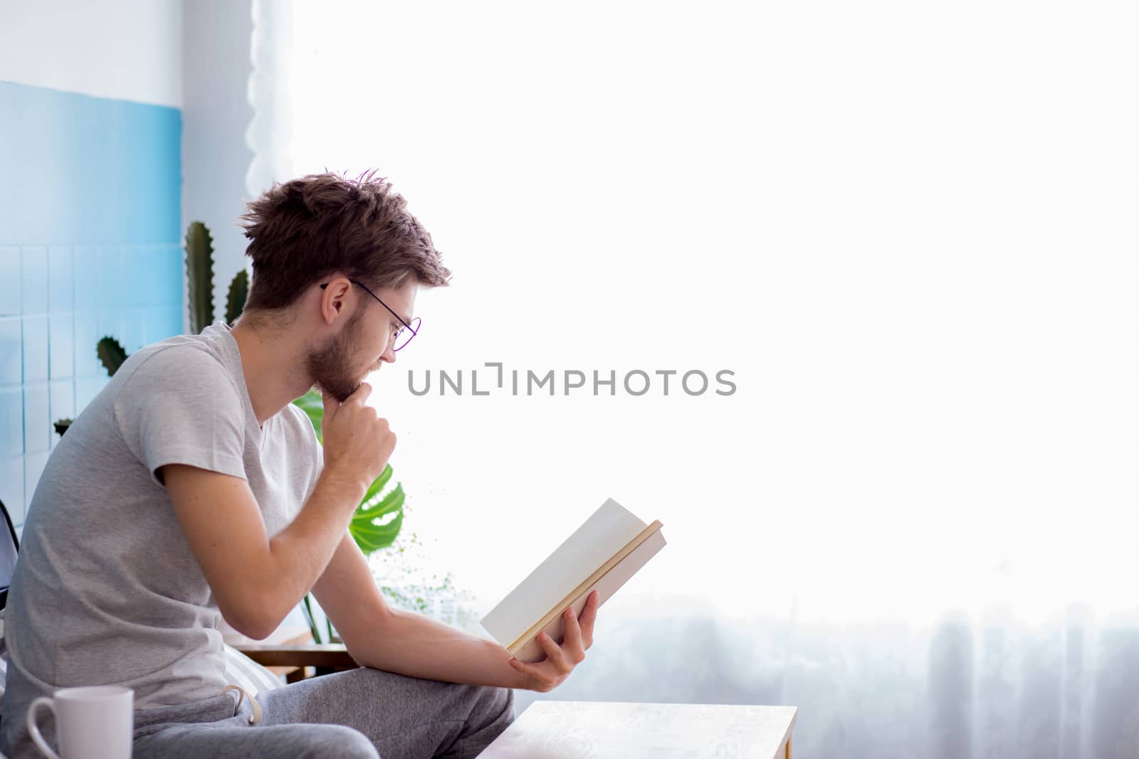 Young man reading book on sofa in the living room.