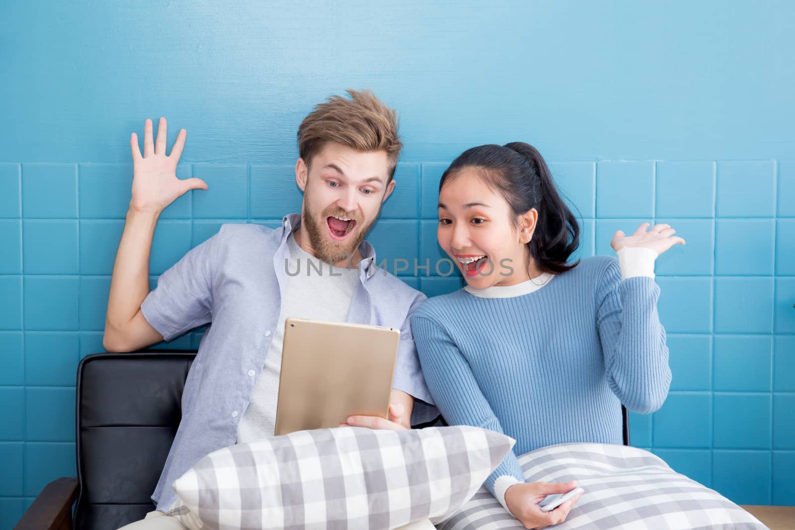 Cute loving couple is using tablet in sofa - They are sitting and smiling and glad with success.
