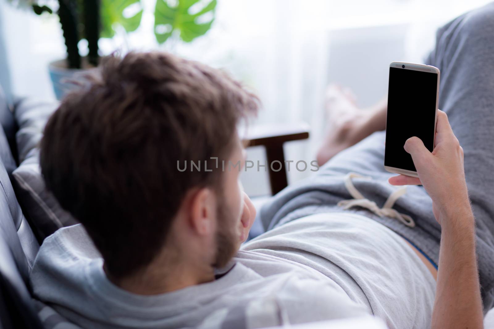 Happy man watching media content in a mobile sitting on a couch at home - Top side view mock up.