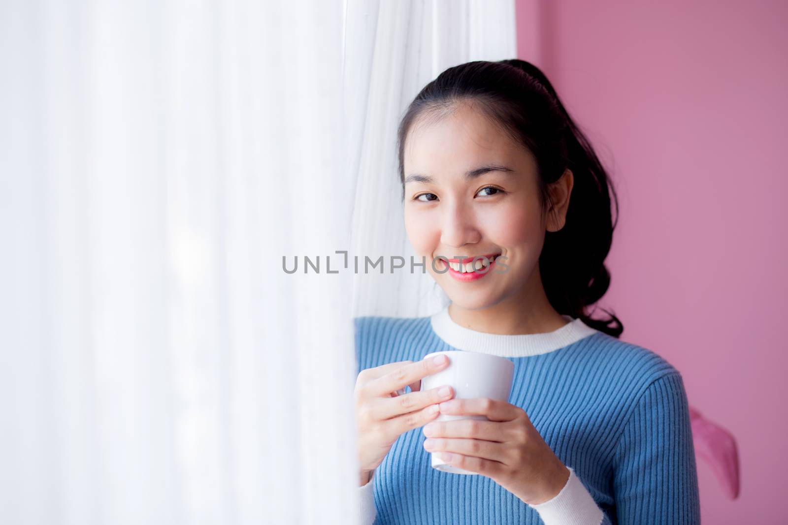 Beautiful young woman is looking out the window and holding a cup of coffee in morning.