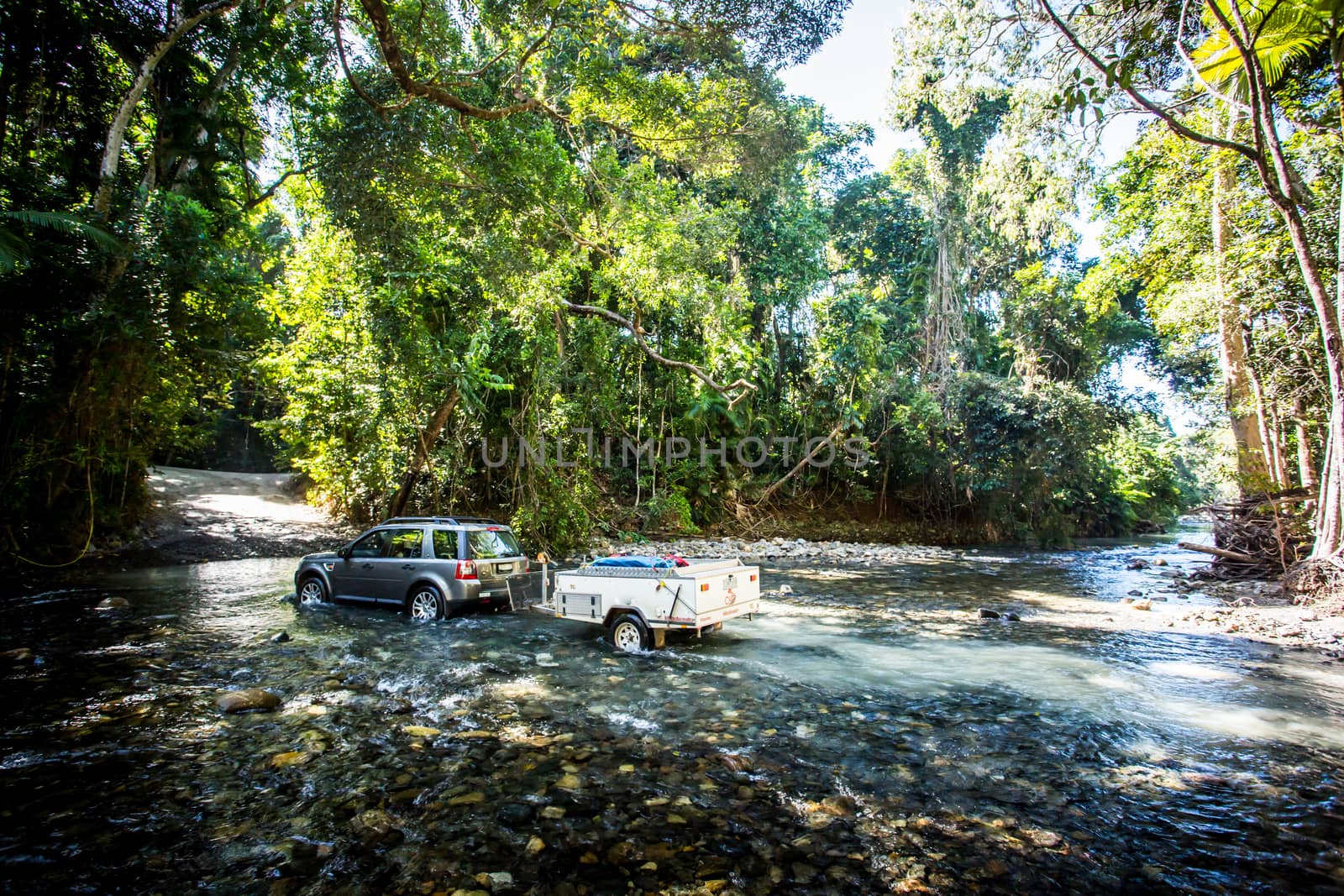 A car drives along Cape Tribulation Rd and crosses a river near Cape Tribulation in the Daintree, Queensland, Australia