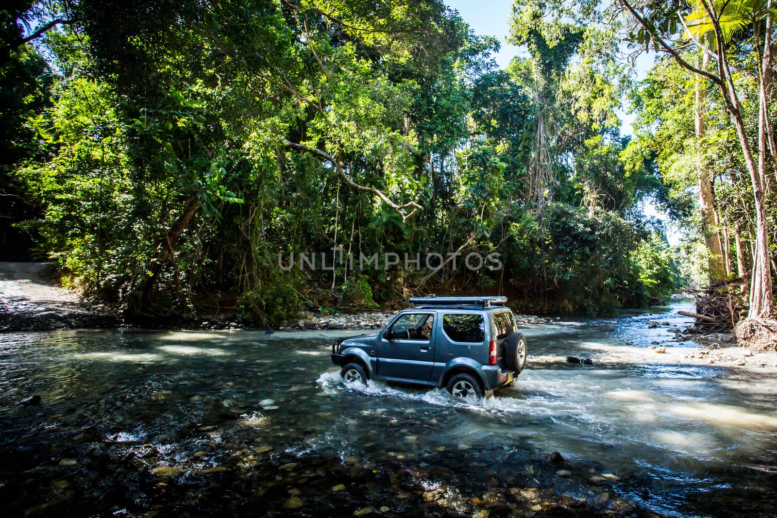 A car drives along Cape Tribulation Rd and crosses a river near Cape Tribulation in the Daintree, Queensland, Australia
