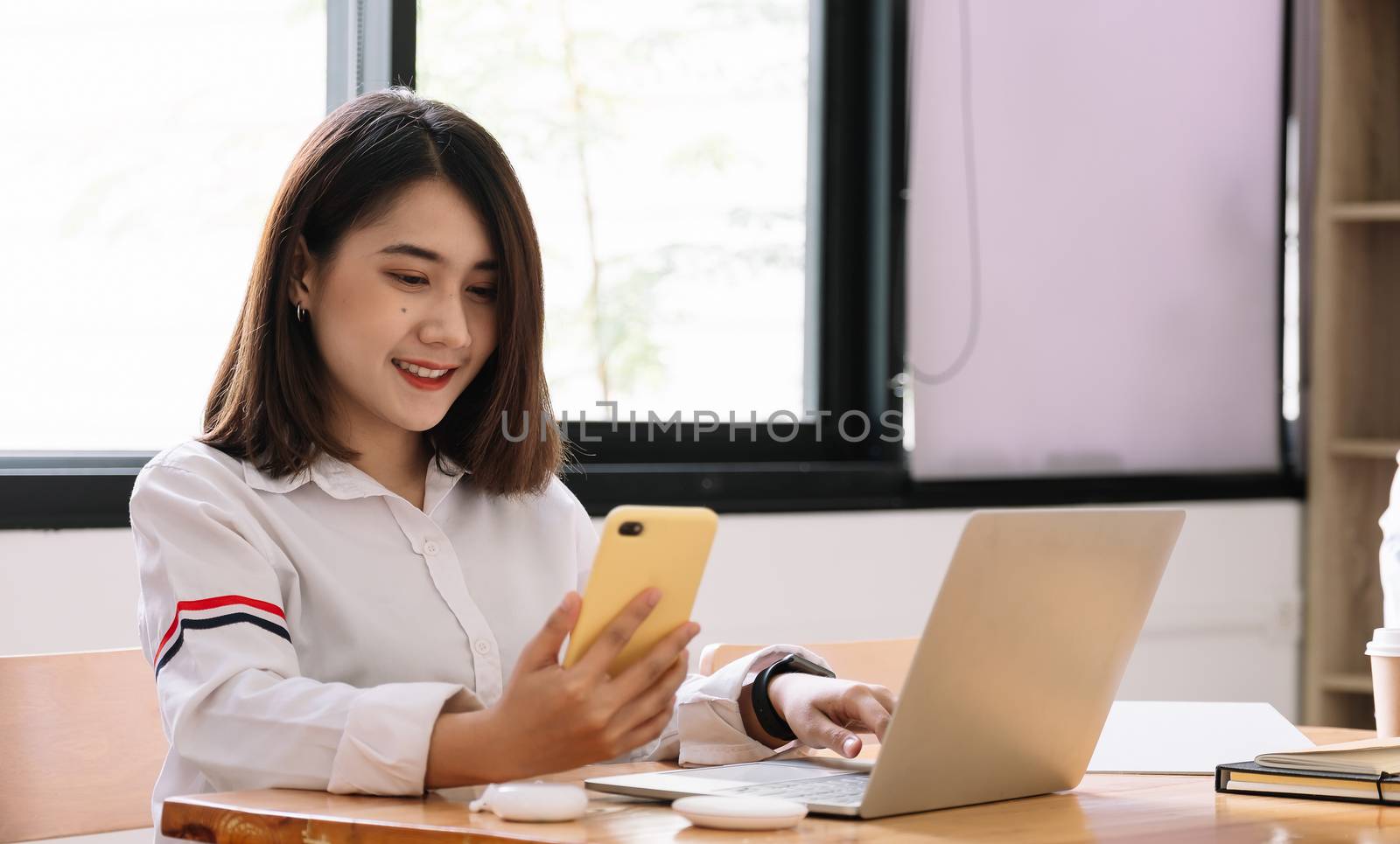 Asian girl works from home or a student is studying from home or a freelancer. She uses a smart phone and laptop computer by nateemee