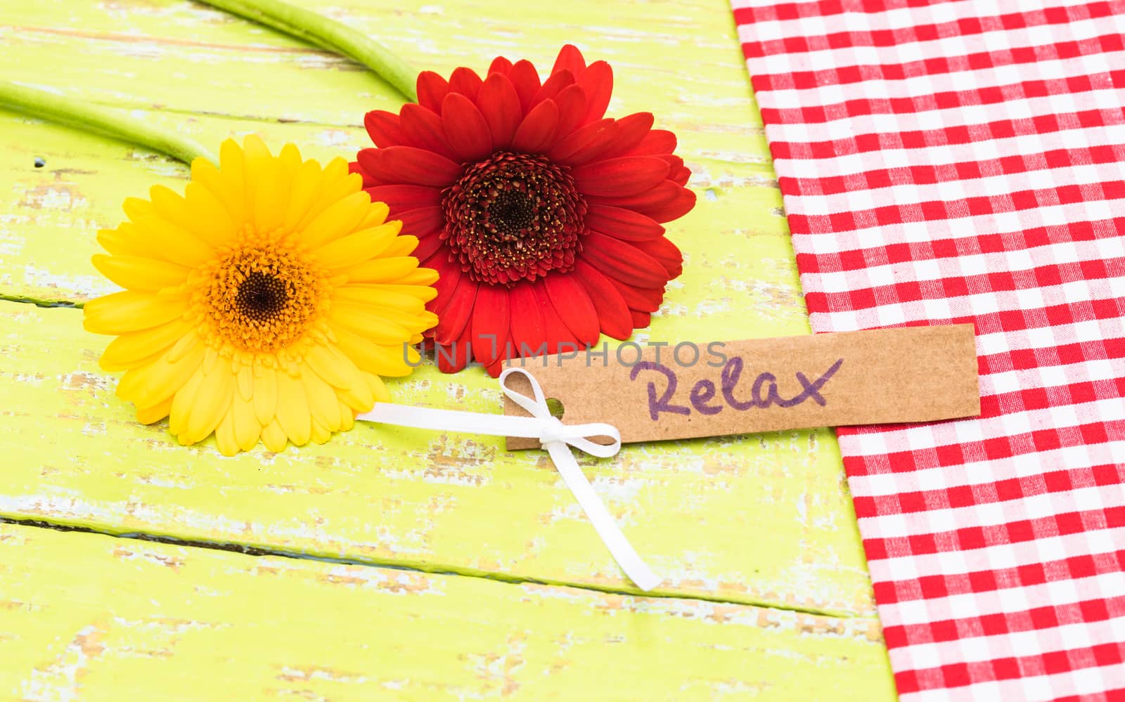 Colorful flowers with tag with the word relax on colored wooden table background