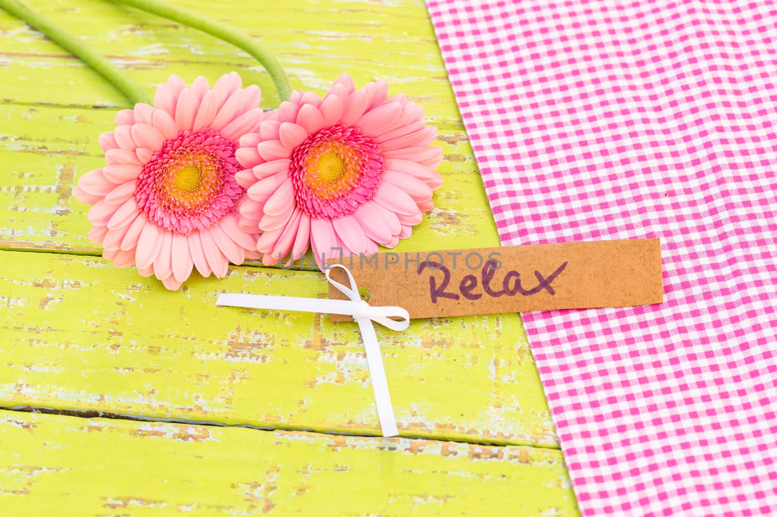 Pastel pink flowers with gift card with the word relax decorated on colored wooden table