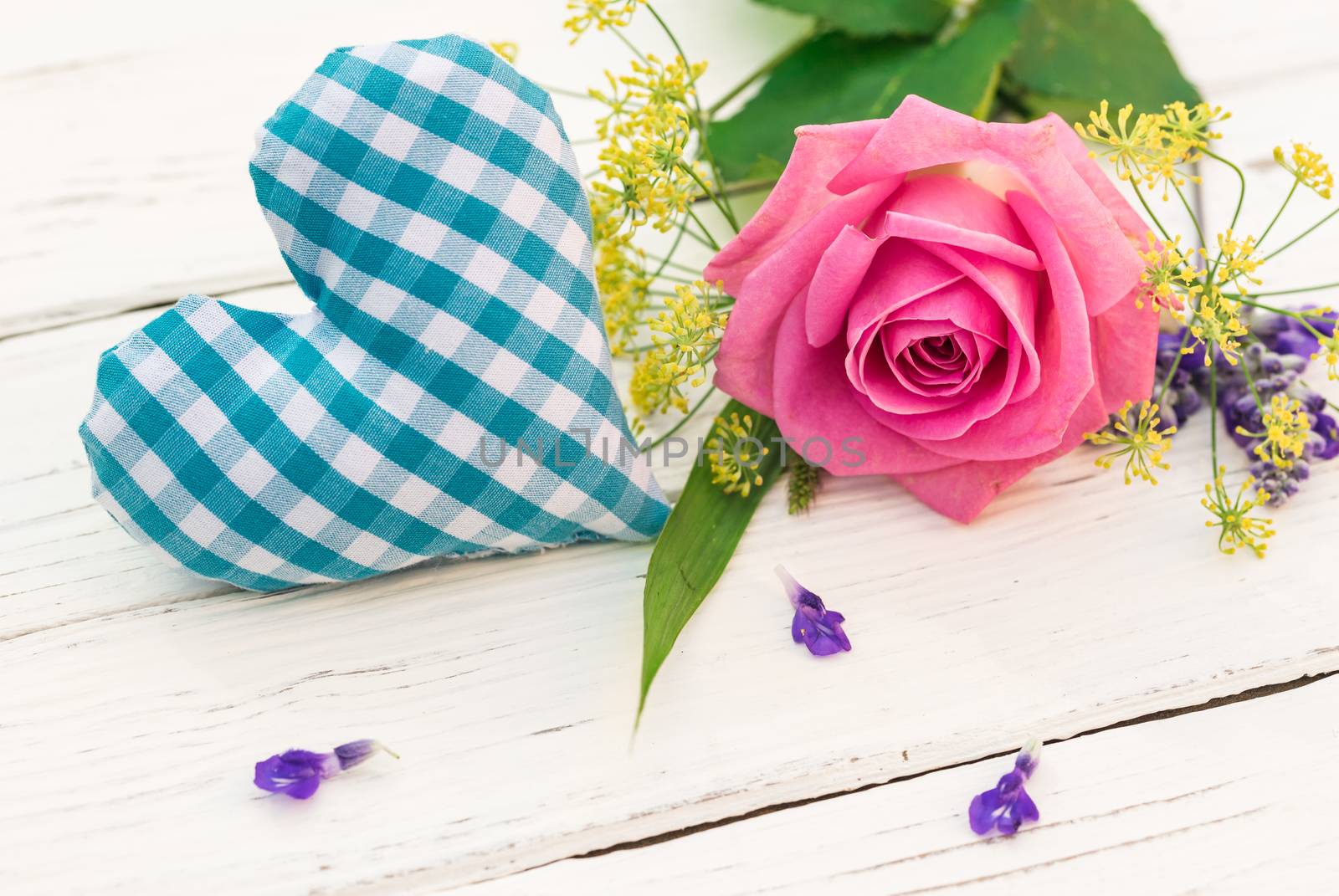 Blue heart with bunch of flowers on white wooden background