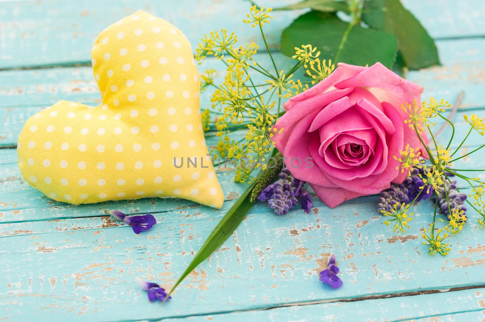 Yellow heart with beautiful pink rose flower, close up on light blue wooden background