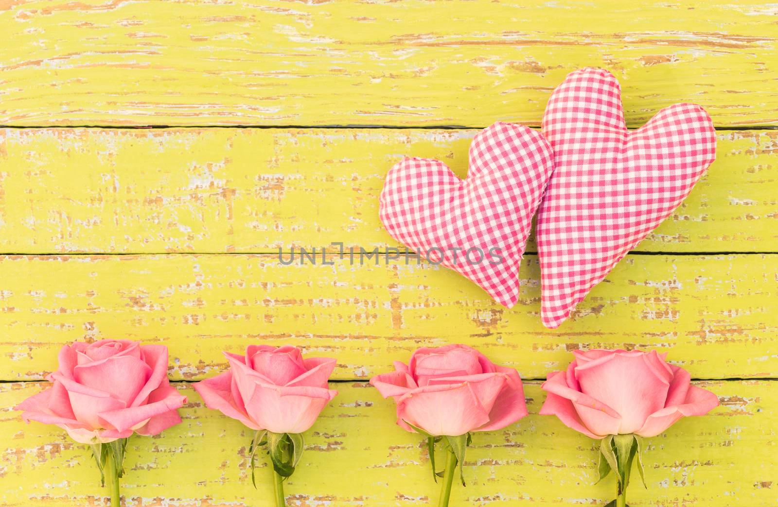 Pink roses flower arrangement with two hearts on yellow wooden background with copy space