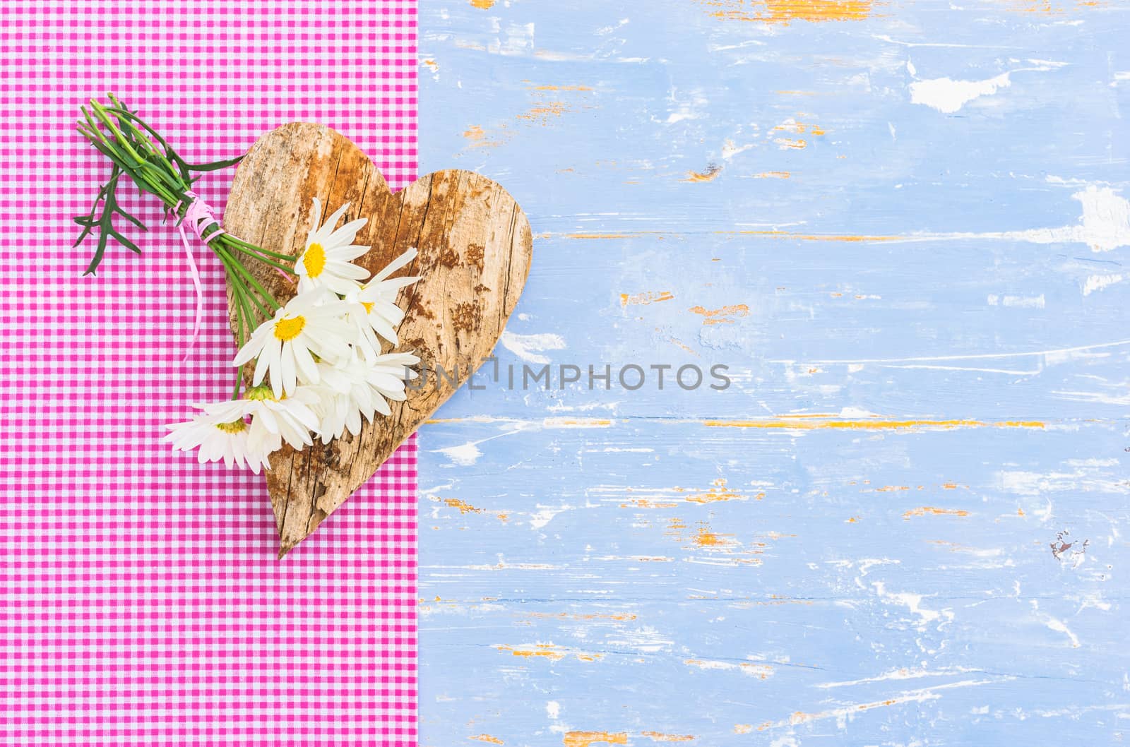 Romantic background with heart and bunch of daisy flowers on blue wooden background with copy space