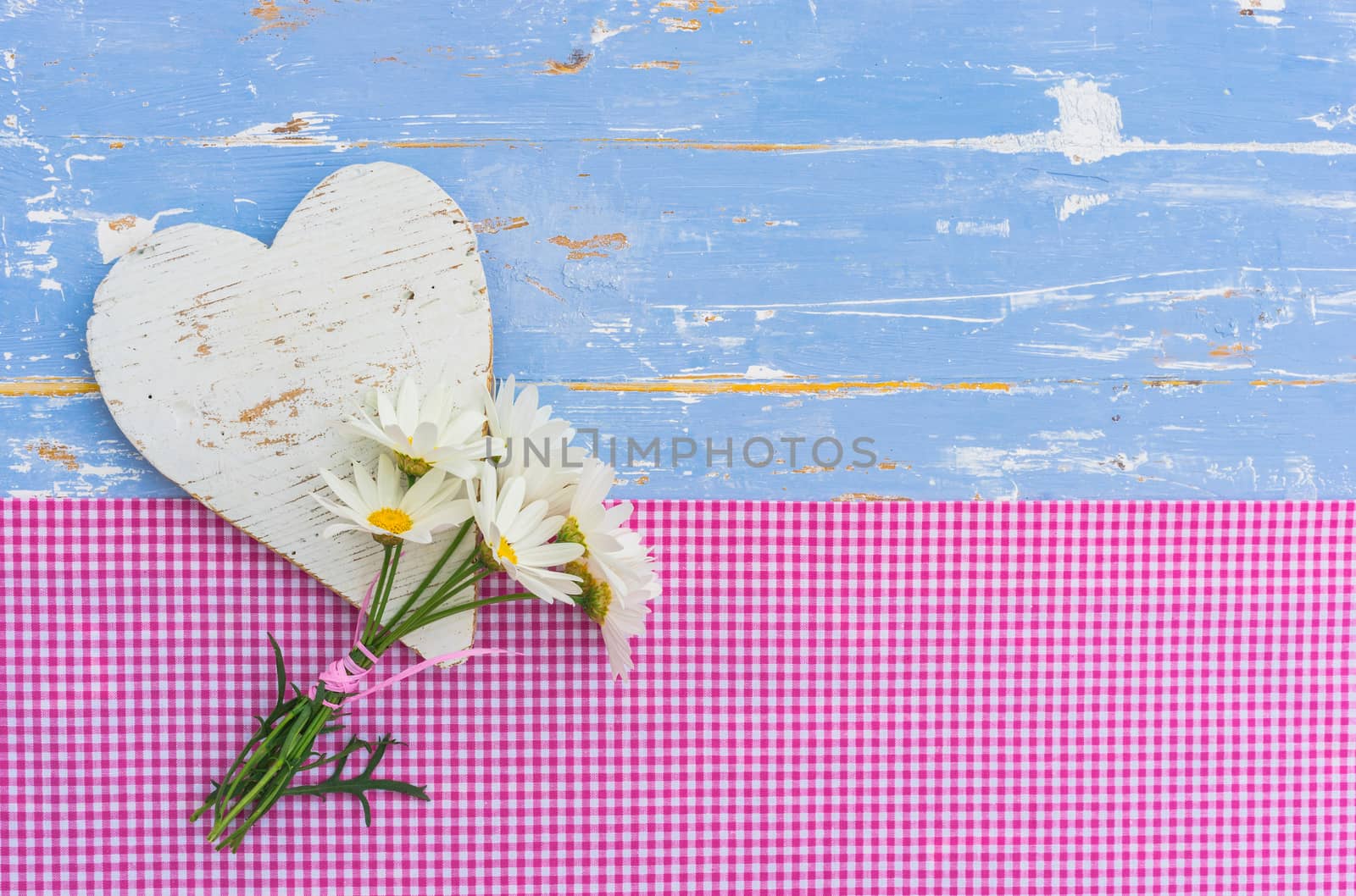 Bunch of daisy marguerite flowers with white heart on blue wooden background with copy space