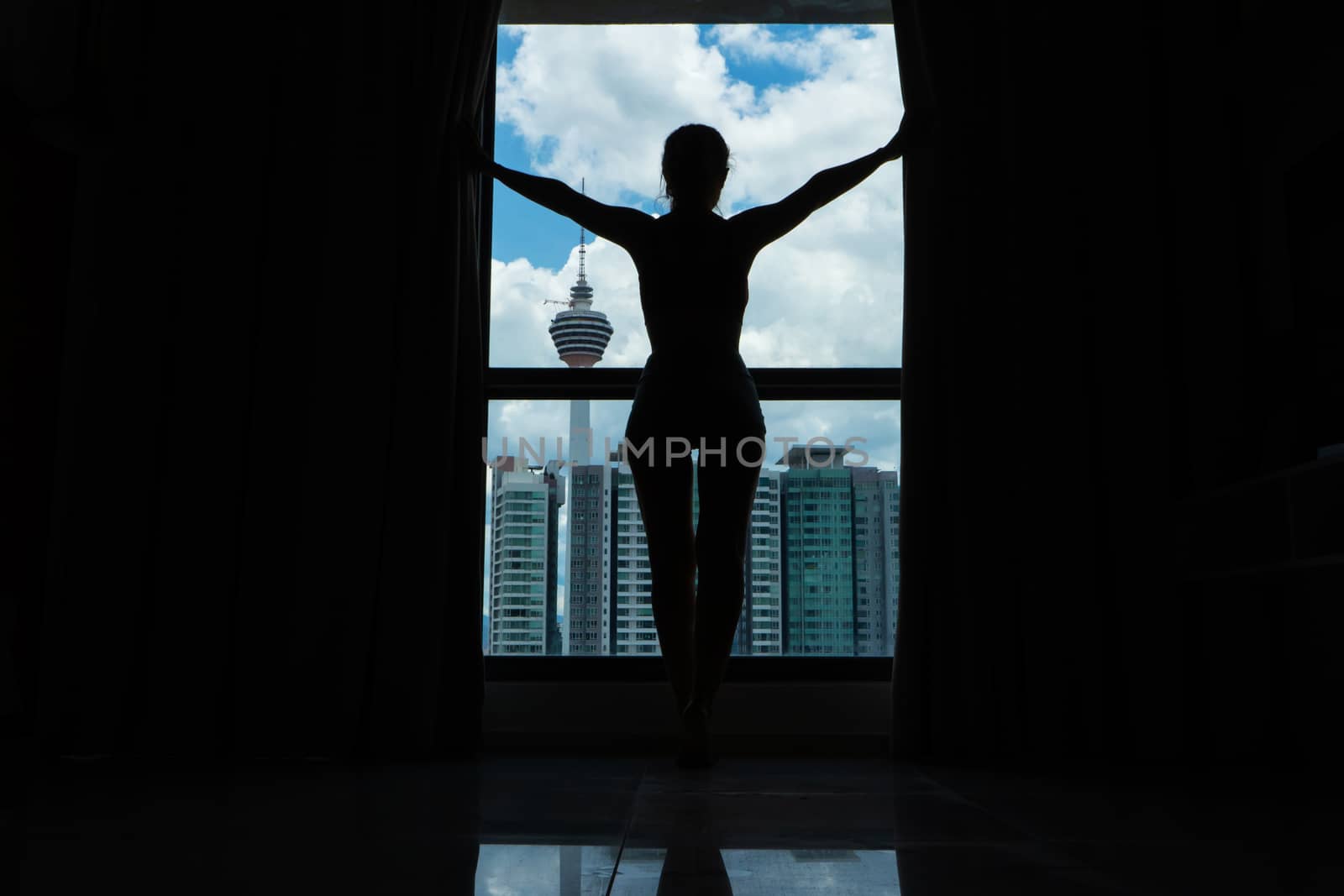 A slender girl is looking at the city through a large window. High floor