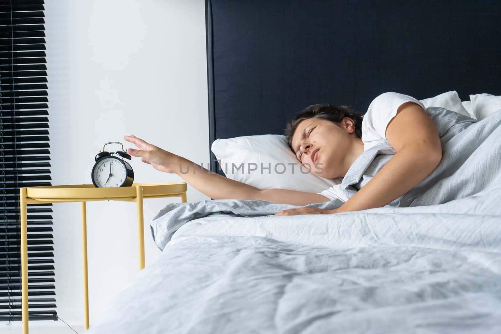 The girl turns off the annoying alarm clock to continue sleeping. Get some more sleep. It a hard morning. Time to wake up