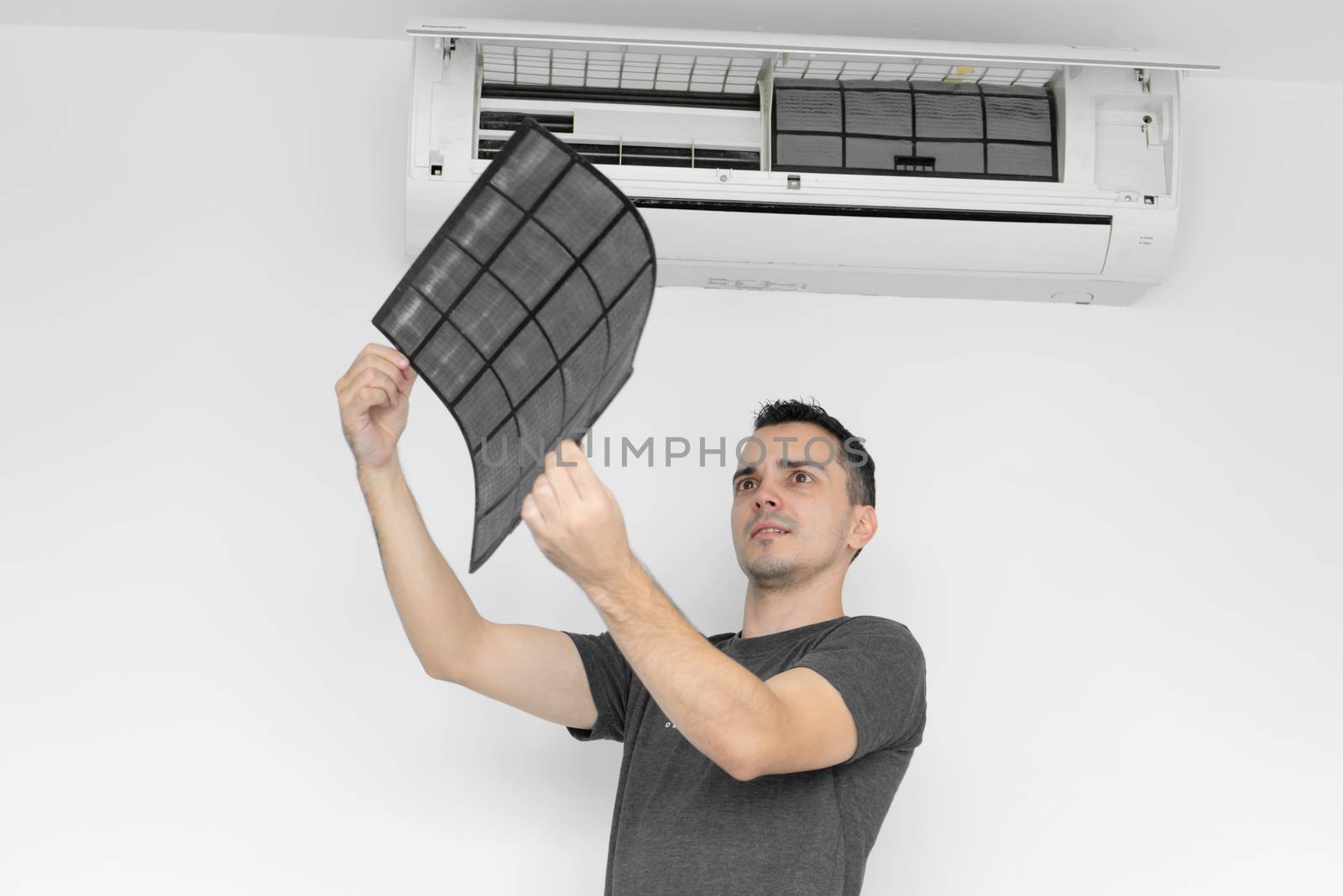 The guy cleans the filter of the home air conditioner from dust. The guy snayed a very dirty air conditioning filter. and examines it in his hands. Climate equipment care