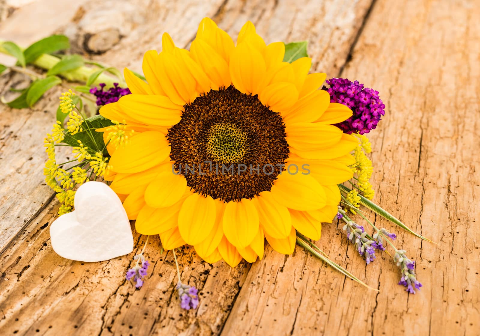 Bunch of flowers with yellow sunflower and little white heart on rustic wooden background
