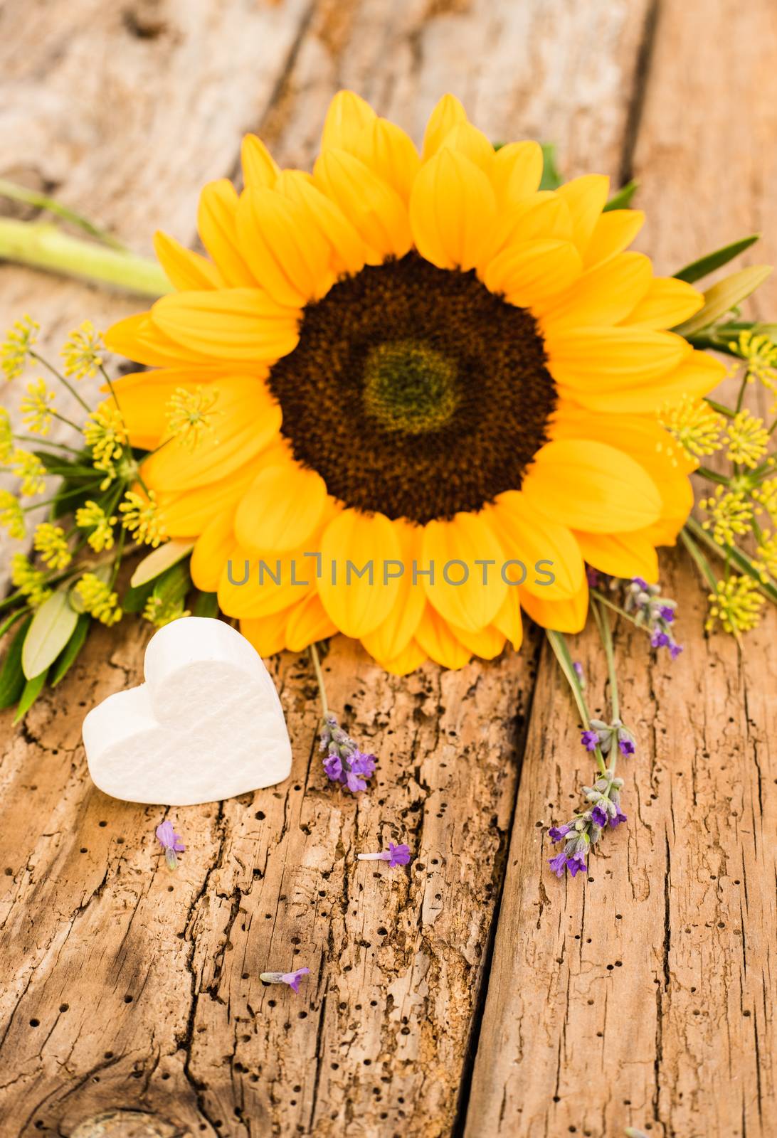 Bunch of flowers with yellow sunflower and little heart on rustic wooden background
