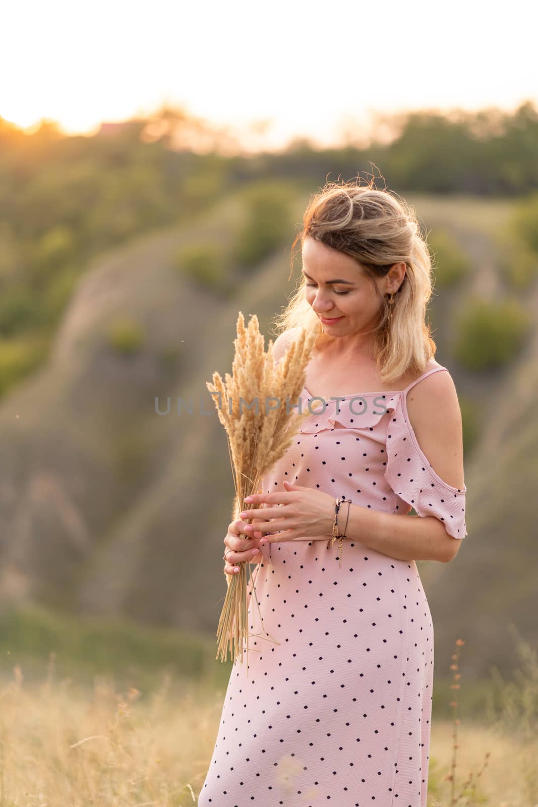 Beautiful tender girl in a white sundress walks at sunset in a field with a spikelet bouquet. by Try_my_best